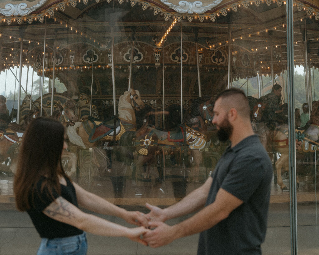 Couple holding hands with Jane's Carousel in the background in Brooklyn, NYC.