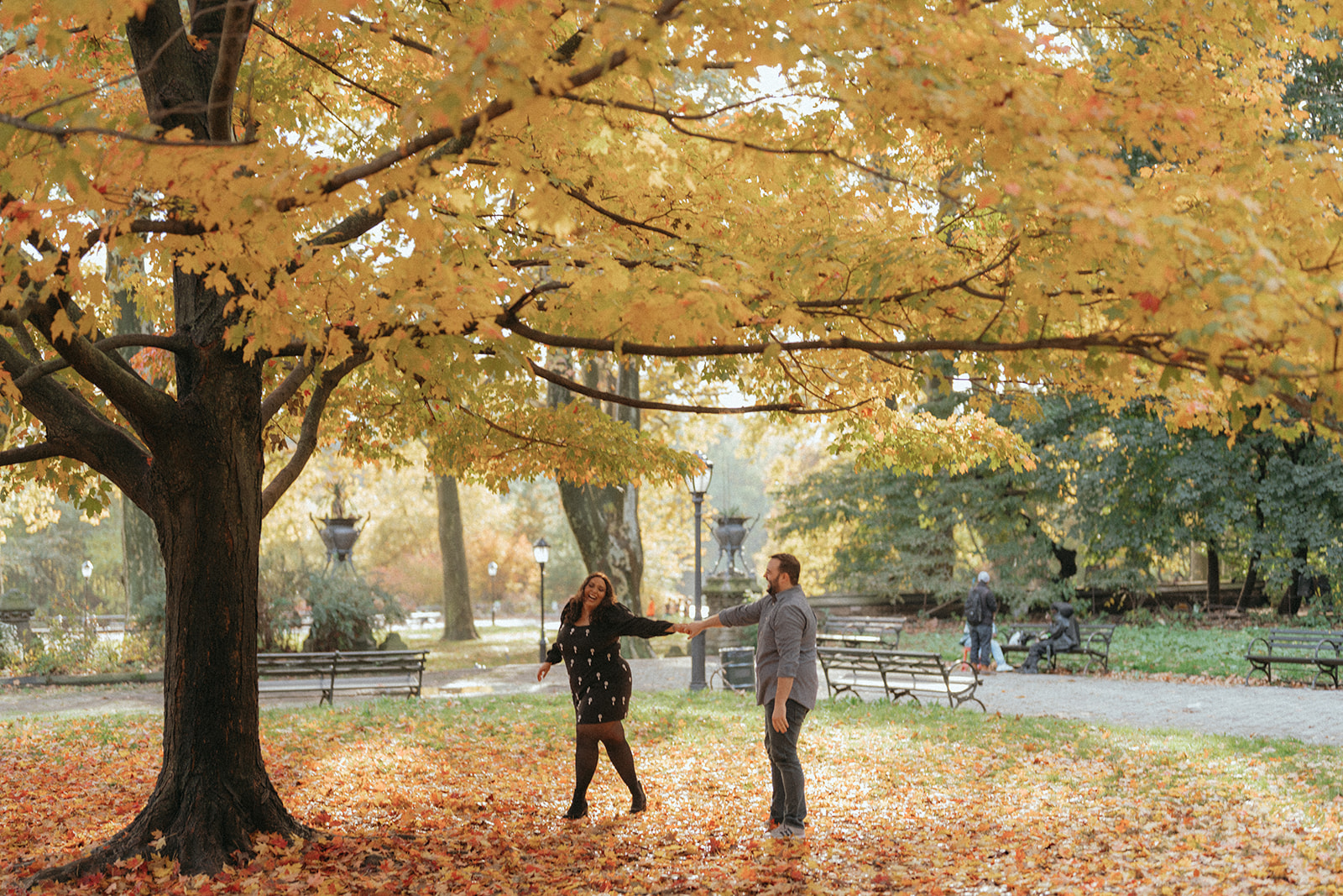 Couple dancing and laughing in Prospect Park in NYC in the fall with colorful fall trees surrounding them. 
