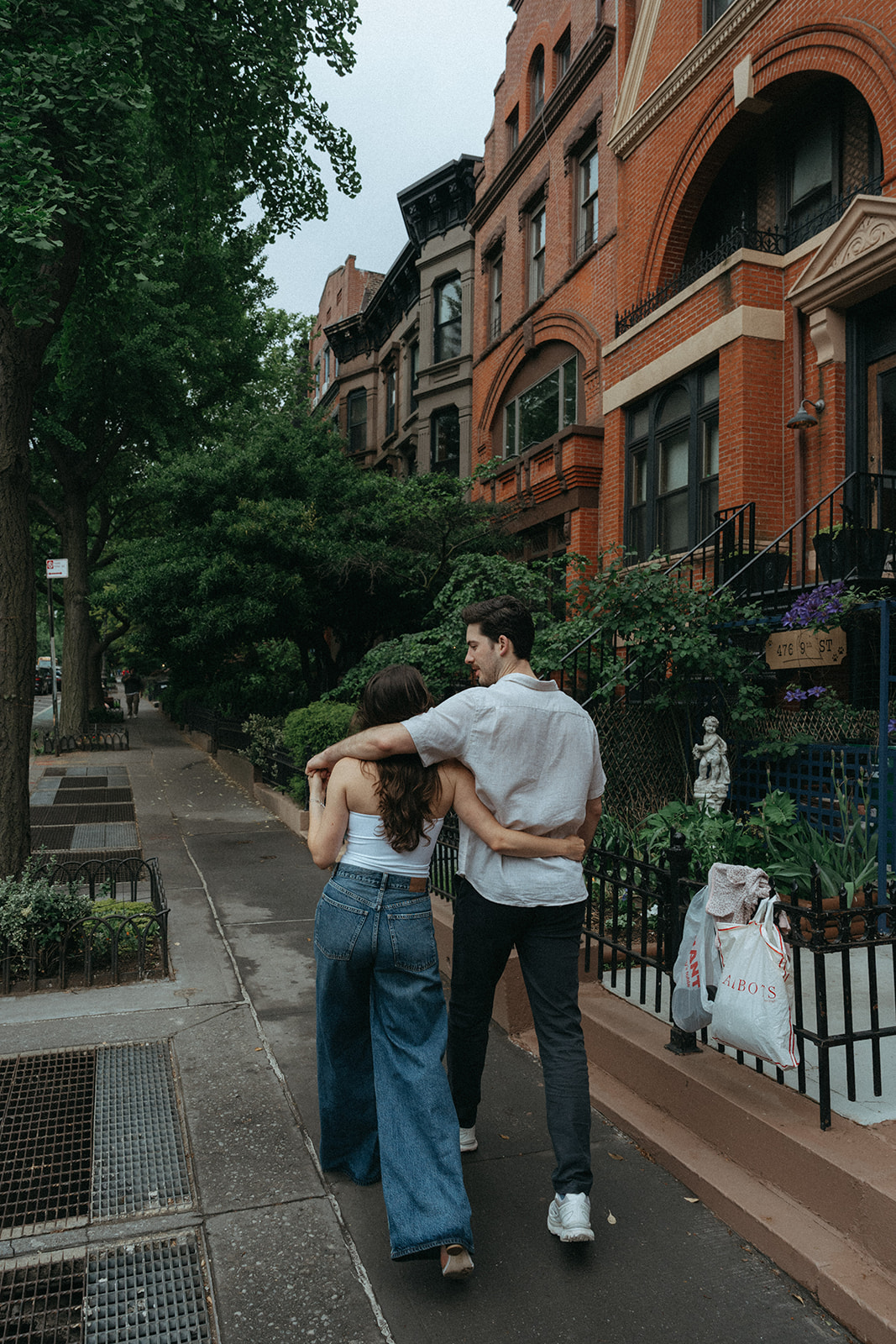 Engaged couple embracing on a leafy brownstone sidewalk in Brooklyn, New York.