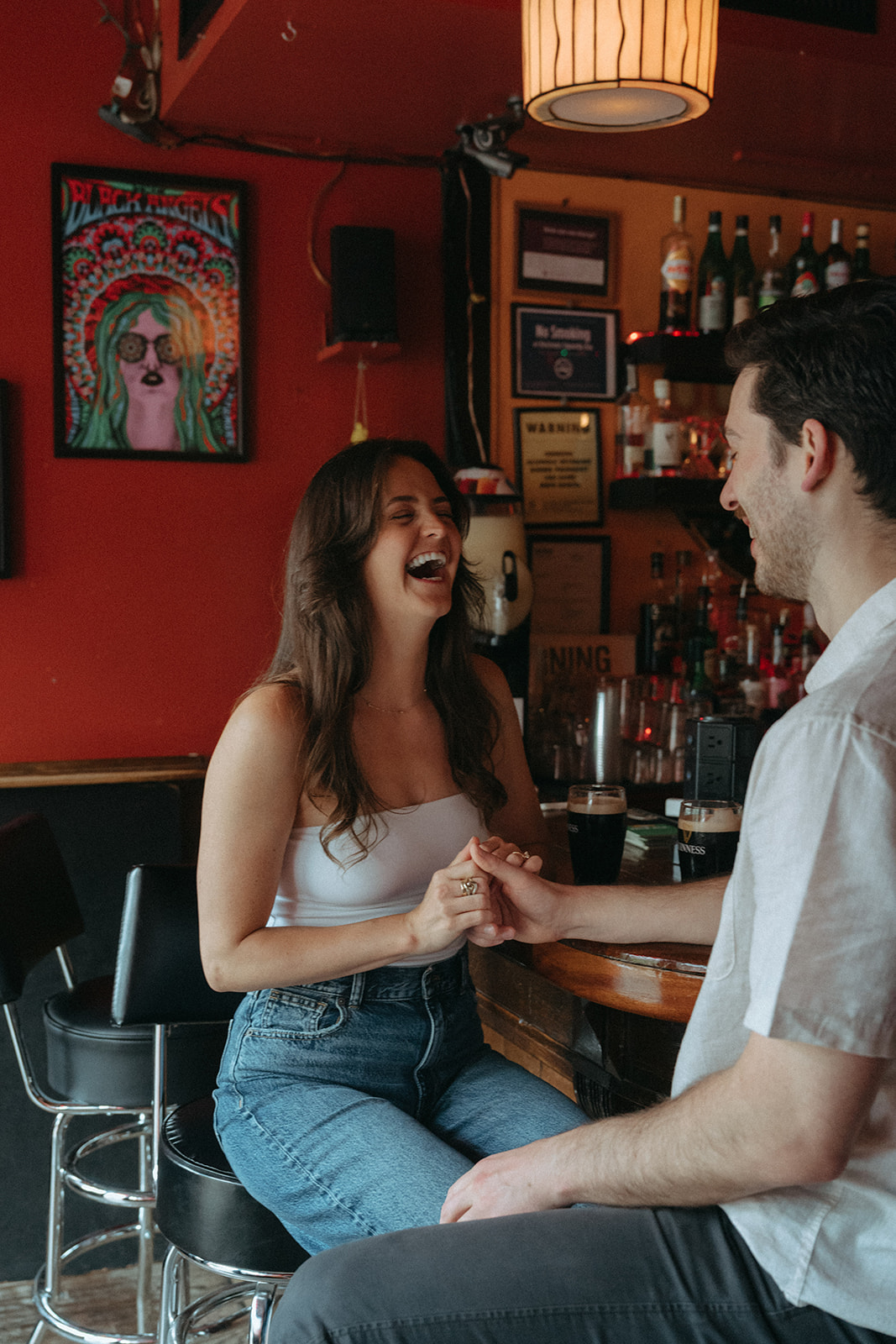 Couple laughing together at a cozy red-walled Brooklyn bar during their engagement session.