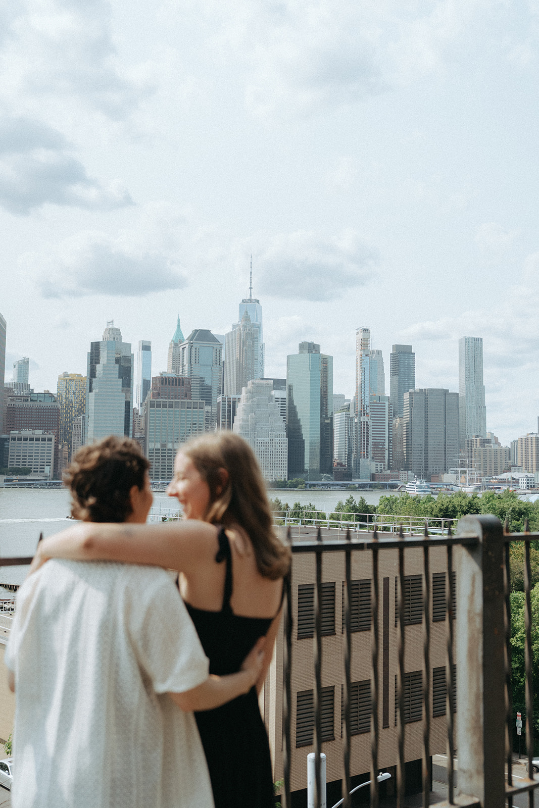 Engaged couple embracing with the Lower Manhattan skyline backdrop at the Brooklyn Heights Promenade.