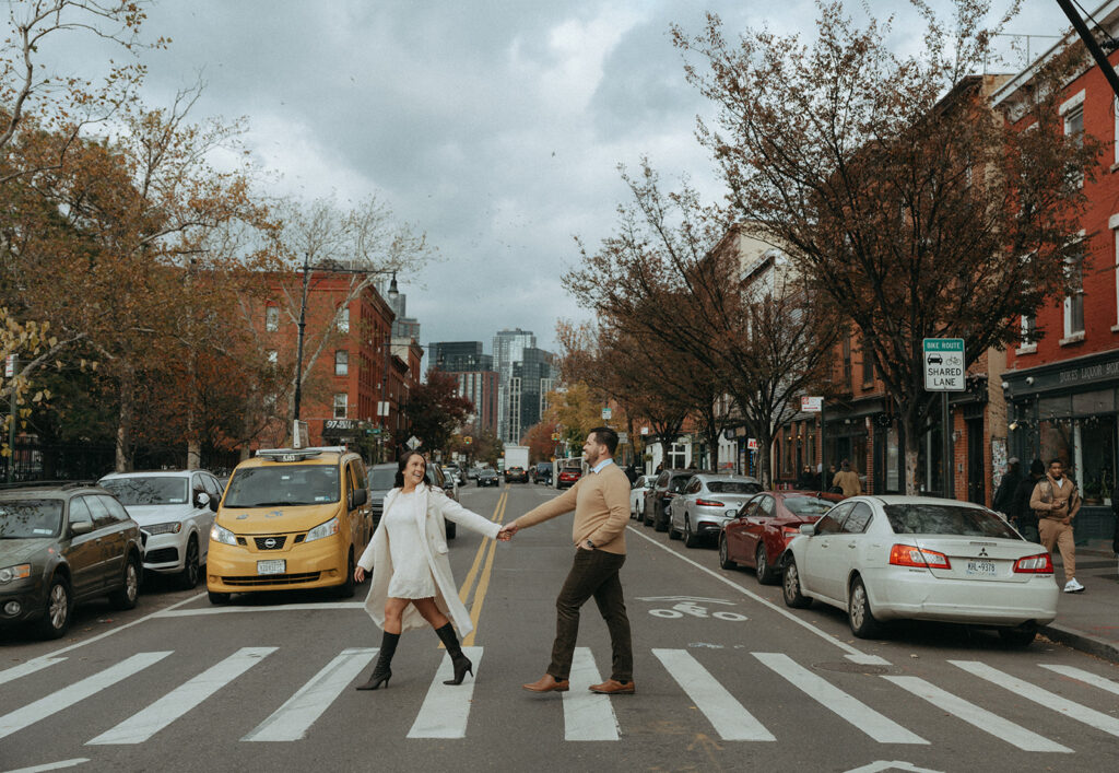 Couple in a Brooklyn crosswalk with a yellow taxi and autumn foliage during their fall engagement photoshoot.