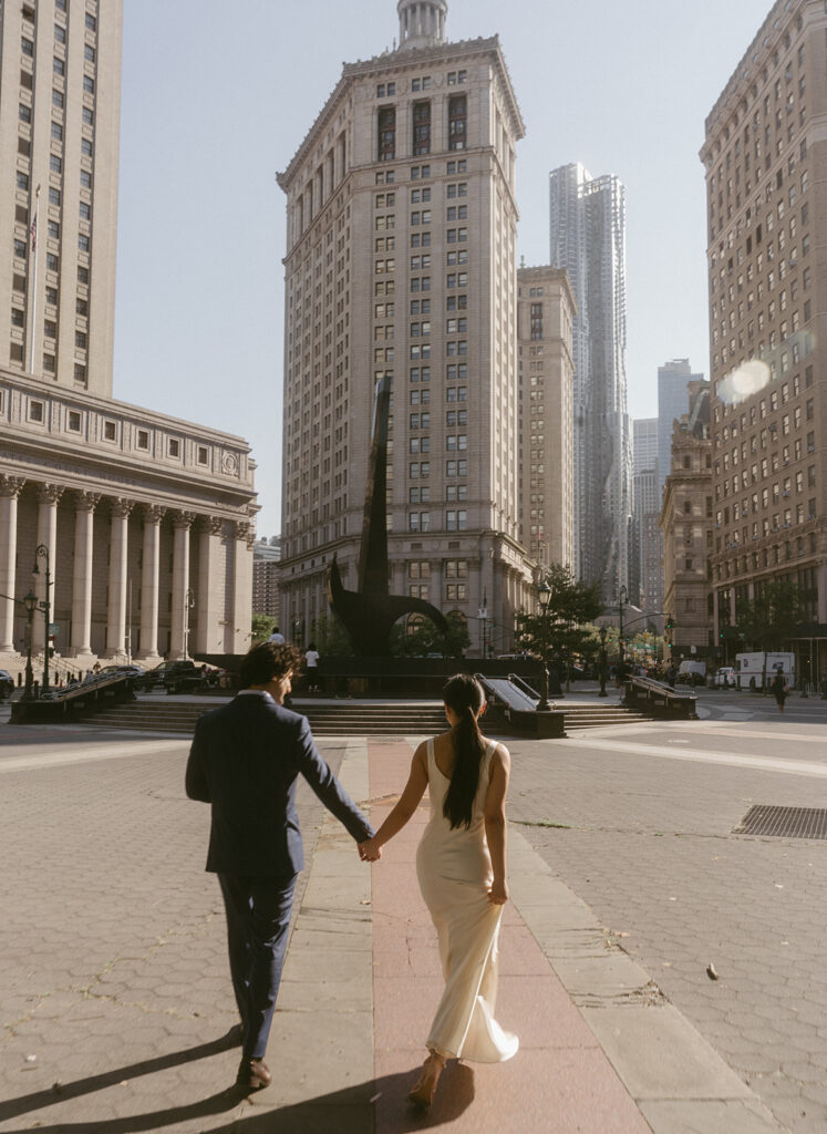 Bride and groom holding hands in streets of NYC in front of City Hall.