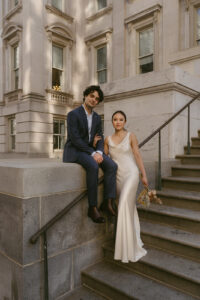 Couple in a blue suit and white satin dress sitting on steps during their New York City elopement