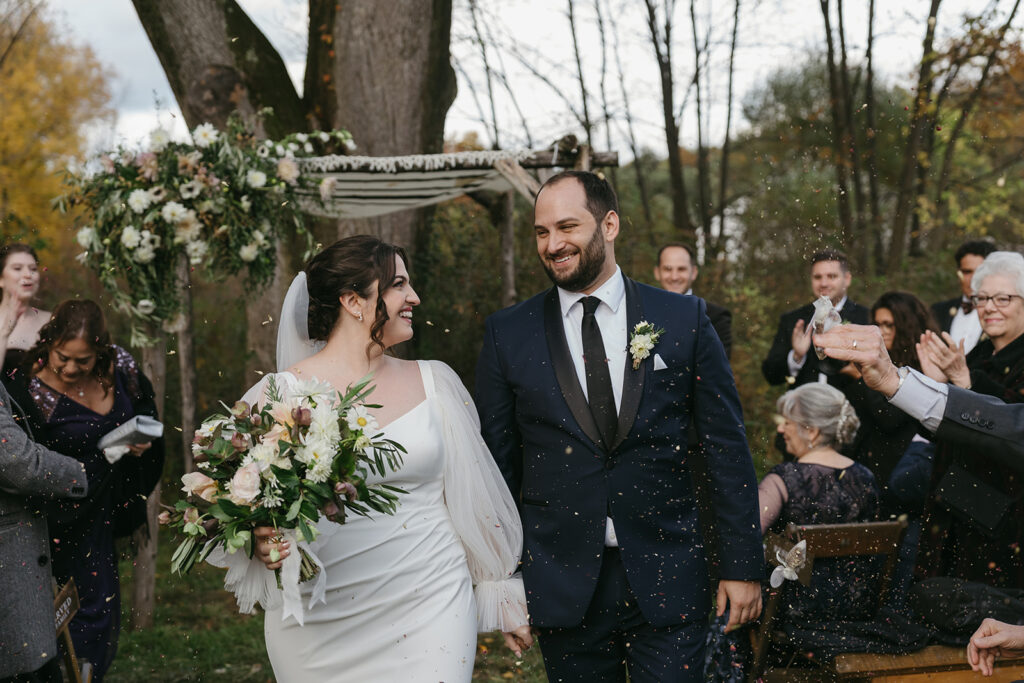 Bride and groom walking up the aisle at their Blooming Hill Farm wedding outdoor ceremony, flower petals being thrown at them