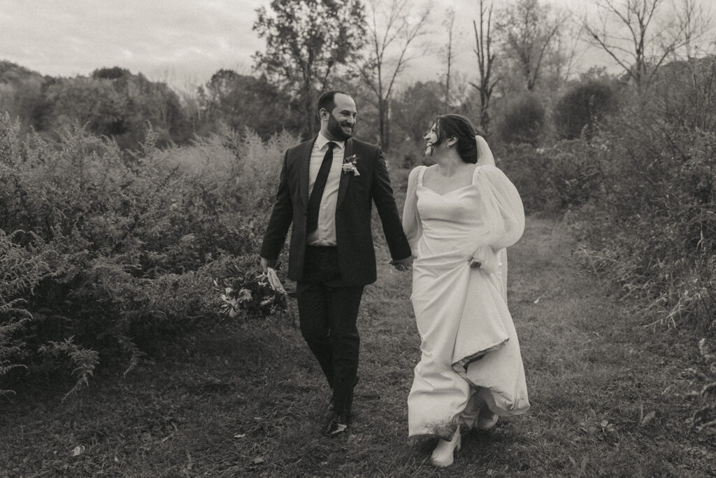 A groom and bride running in a field during their Blooming Hill Farm wedding.