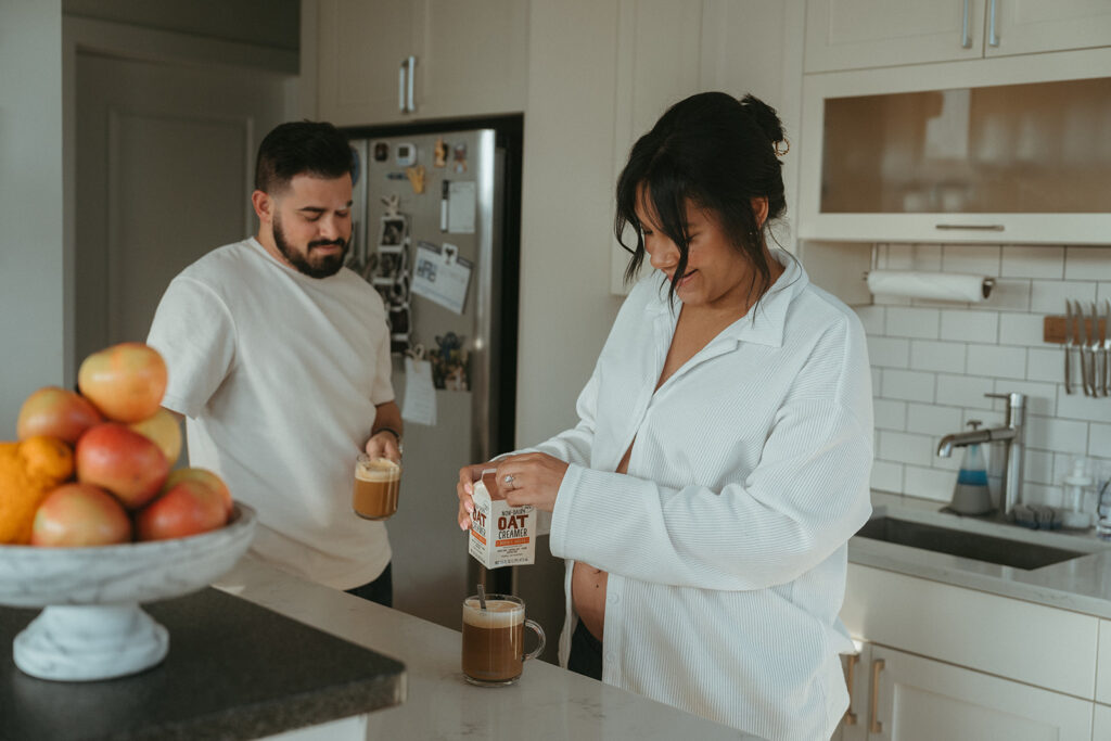 A husband and pregnant wife making coffee in their NYC apartment kitchen.