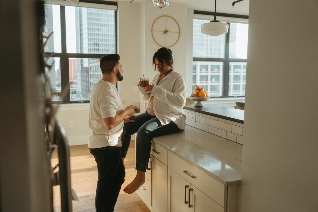 A husband and pregnant wife making coffee in their NYC apartment kitchen.