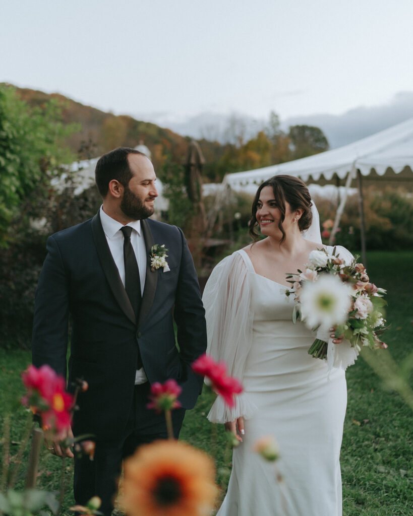 A groom and bride strolling through flower fields during their Blooming Hill Farm wedding.