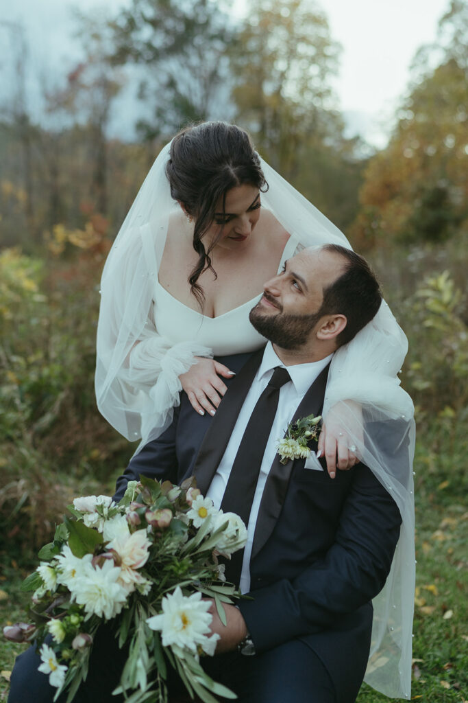 A groom and bride embracing in a field during their Blooming Hill Farm wedding.