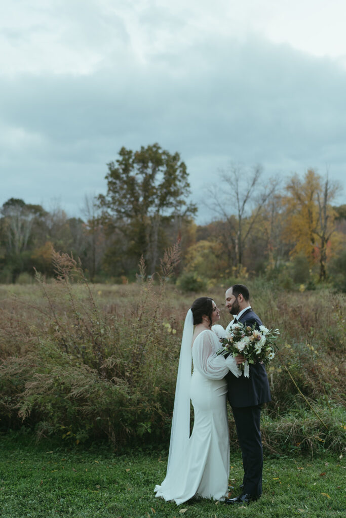 A groom and bride embracing in a field during their Blooming Hill Farm wedding.