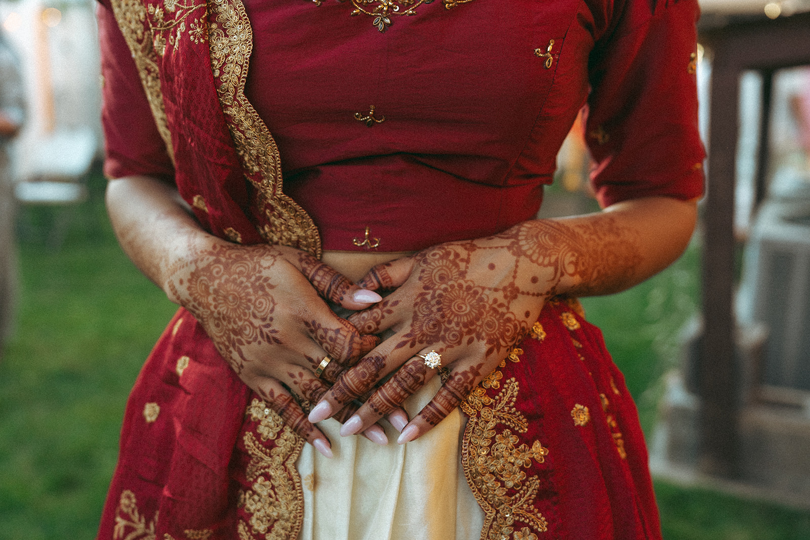 Close-up of bride’s henna-covered hands resting on her red and gold saree — Elsie Goodman Photography.