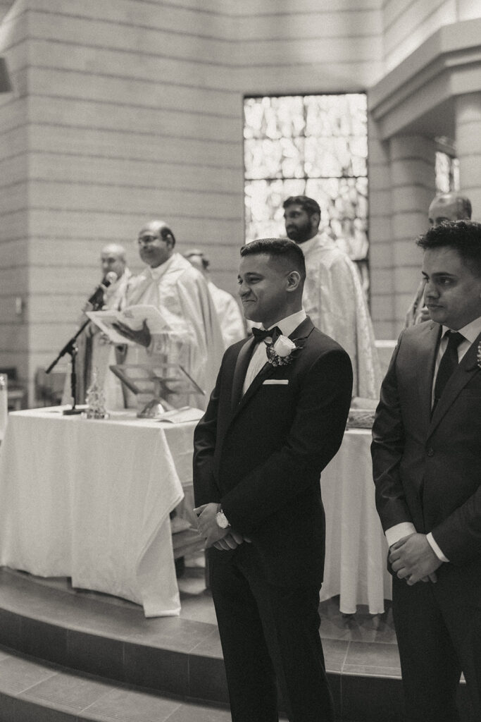 The groom smiles with emotion while waiting at the altar for his bride during a Catholic Indian wedding ceremony, a touching moment preserved by Elsie Goodman Photography for an Indian wedding photo gallery.