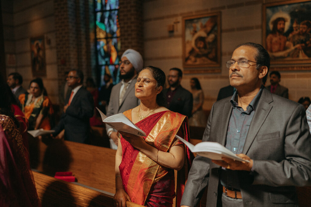 Guests in colorful Indian attire singing hymns during the Indian Catholic wedding ceremony, adding cultural richness to the Long Island wedding, captured by Elsie Goodman Photography.