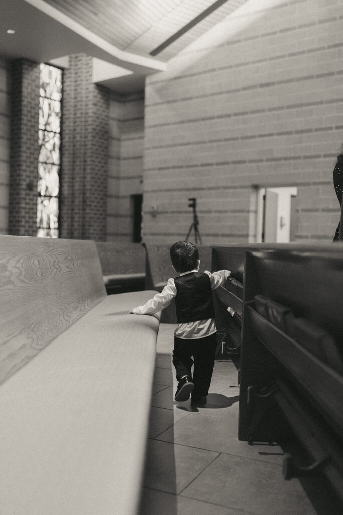 A young ring bearer in a vest wanders down the church aisle after the Catholic Indian wedding ceremony, a sweet candid captured by Elsie Goodman Photography for an Indian wedding photo gallery.