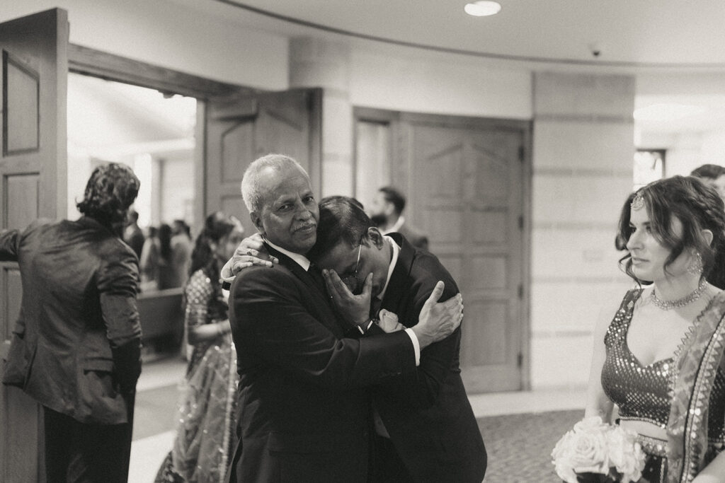 Emotional moment between two men sharing a tearful embrace after the Catholic Indian wedding ceremony at Our Lady of the Snows Church, captured authentically by Elsie Goodman Photography for this Indian wedding photo gallery.