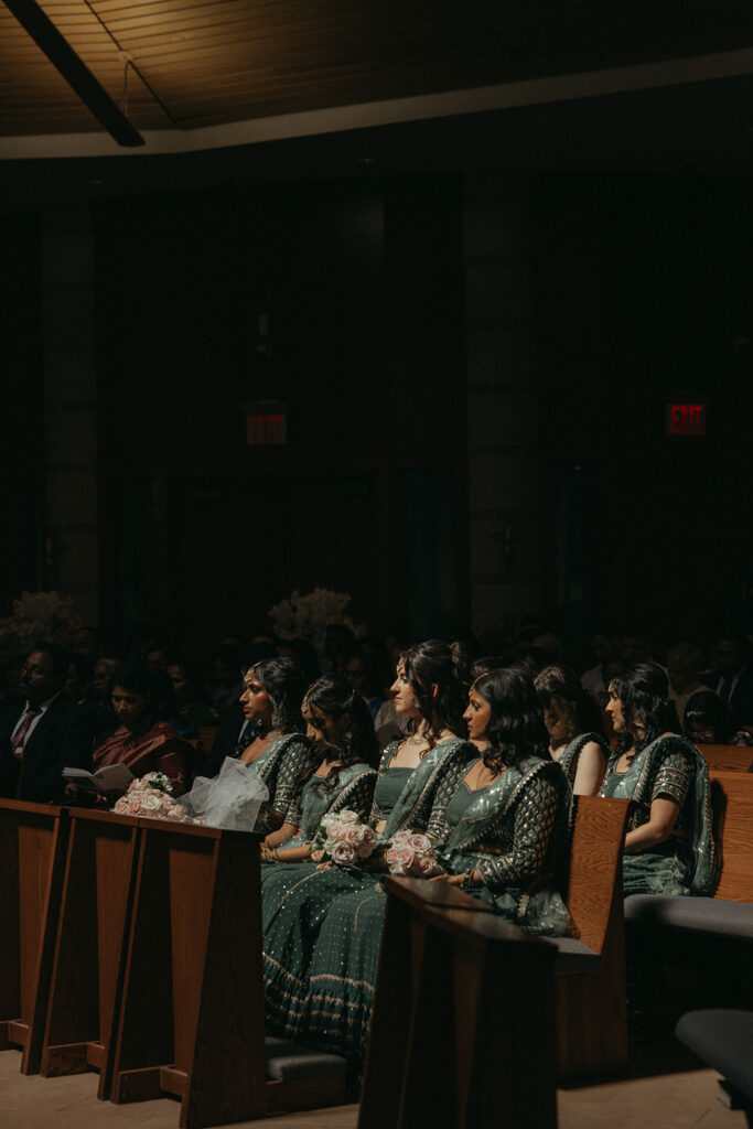 A row of bridesmaids holding pink rose bouquets sits in solemn attention during the Catholic Indian wedding ceremony, an elegant moment captured by Elsie Goodman Photography for an Indian wedding photo gallery.
