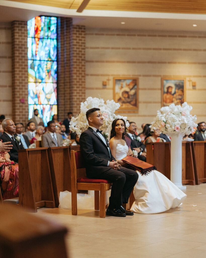 The bride and groom sit side by side at the altar during their Catholic Indian wedding ceremony, a serene scene captured by Elsie Goodman Photography for an Indian wedding photo gallery.