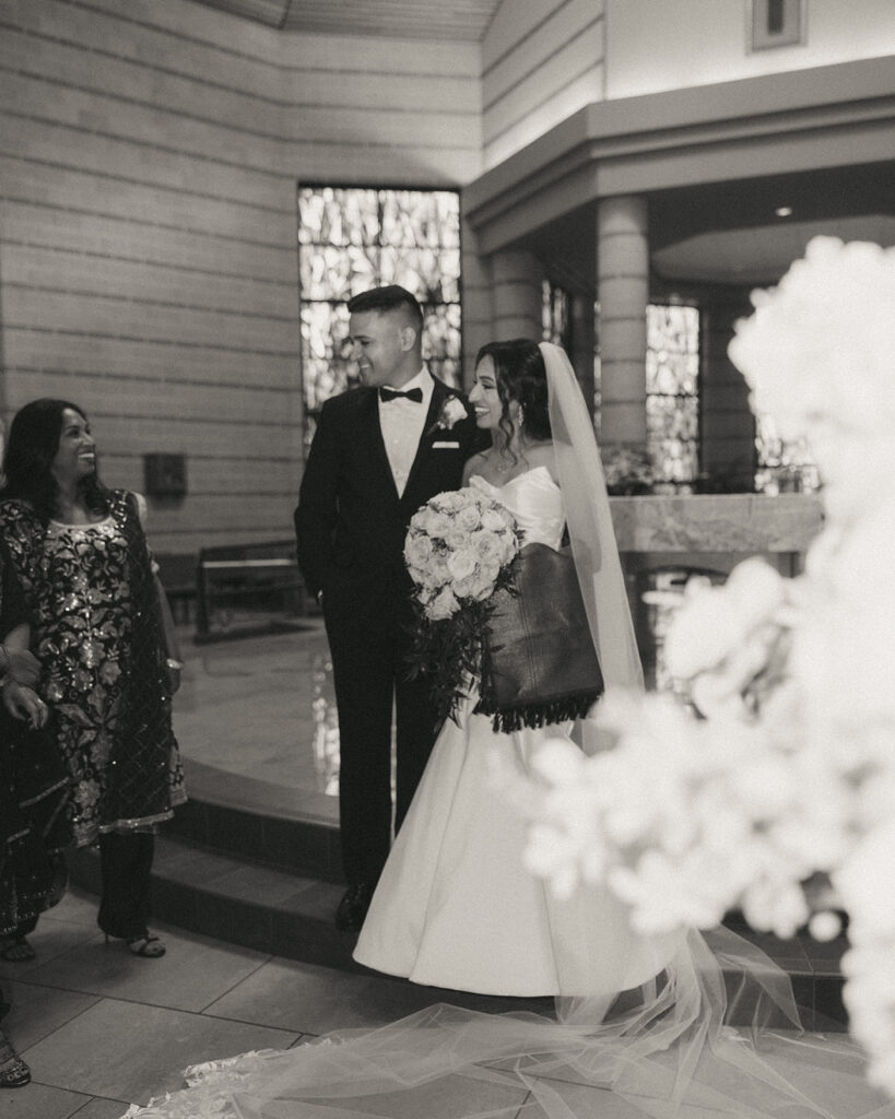 Joyful black and white candid of the bride and groom laughing with family inside the church after their Indian Catholic wedding ceremony, captured in Elsie Goodman Photography’s Indian wedding photo gallery.