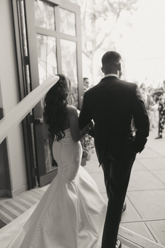 Black and white candid moment of the bride’s flowing veil and gown as she and the groom step outside the church after their Catholic Indian wedding ceremony, captured by Elsie Goodman Photography.