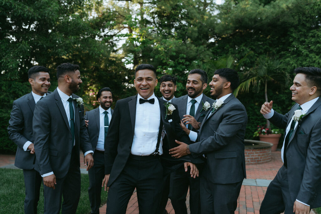 Groom laughing with his groomsmen, captured during playful Indian Catholic wedding party portraits outdoors by Elsie Goodman Photography.