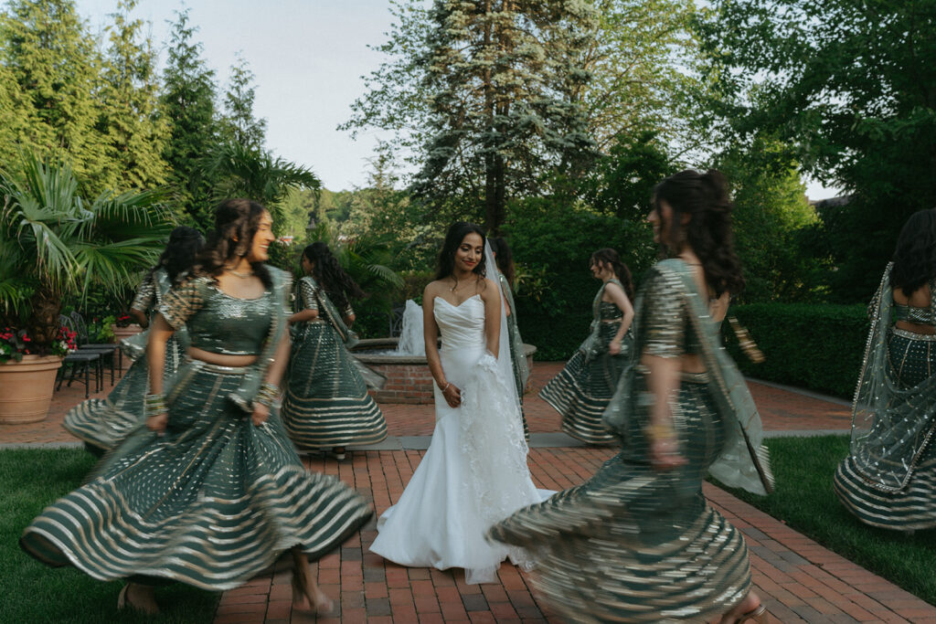 Bride and bridesmaids twirling together in emerald green lehengas, a joyful moment during Indian Catholic wedding party portraits by Elsie Goodman Photography.