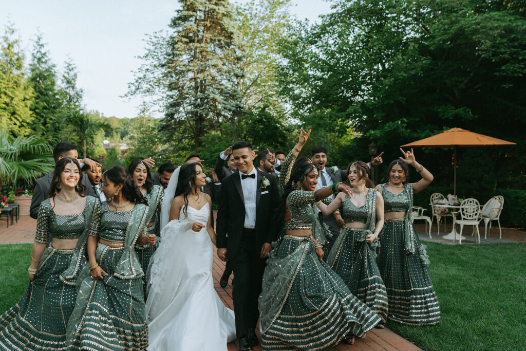 Bride and groom smiling at each other while surrounded by laughing wedding party members during vibrant Indian Catholic wedding party photos by Elsie Goodman Photography.