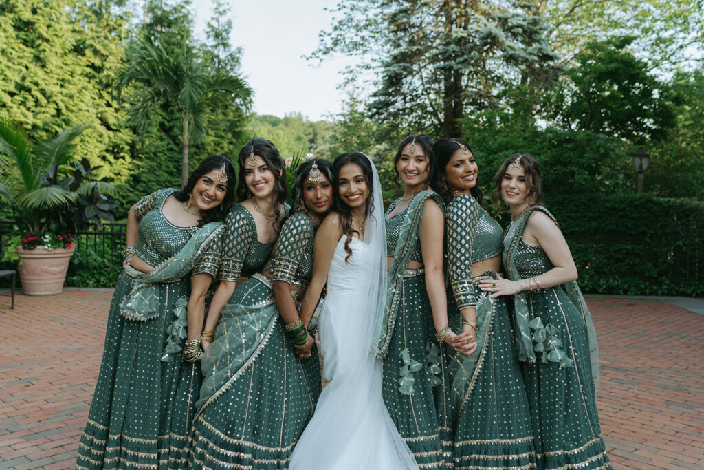 Bride laughing and hugging her bridesmaids dressed in coordinating Indian Catholic wedding dresses during joyful group portraits by Elsie Goodman Photography.
