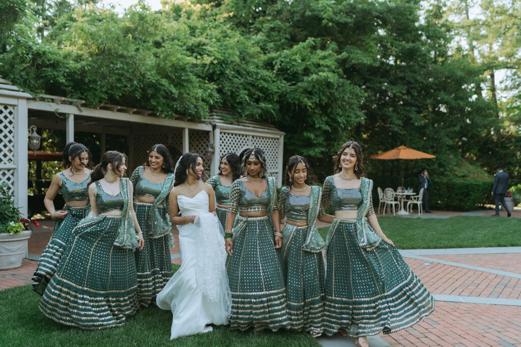 Bride walking hand in hand with her bridesmaids in matching green lehengas, an elegant Indian Catholic wedding moment captured by Elsie Goodman Photography.