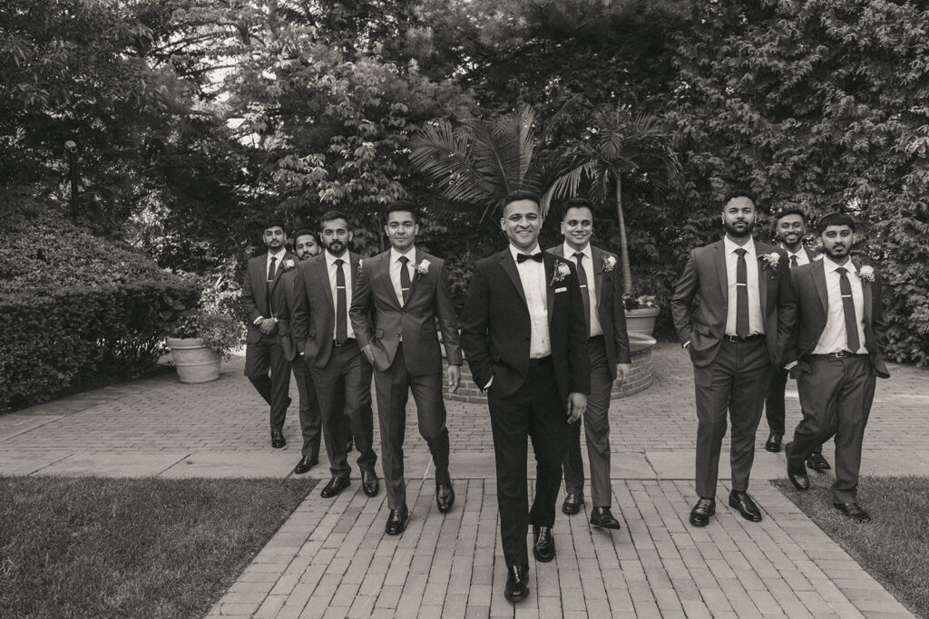 Groom leading groomsmen in a confident walk outdoors, captured by Elsie Goodman Photography at a stylish Indian Catholic wedding.