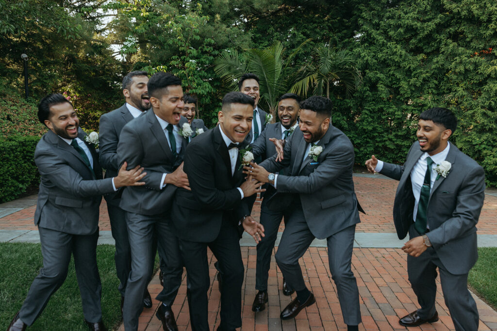 Groom and groomsmen laughing together outdoors, celebrating during Indian Catholic wedding photos captured by Elsie Goodman Photography.