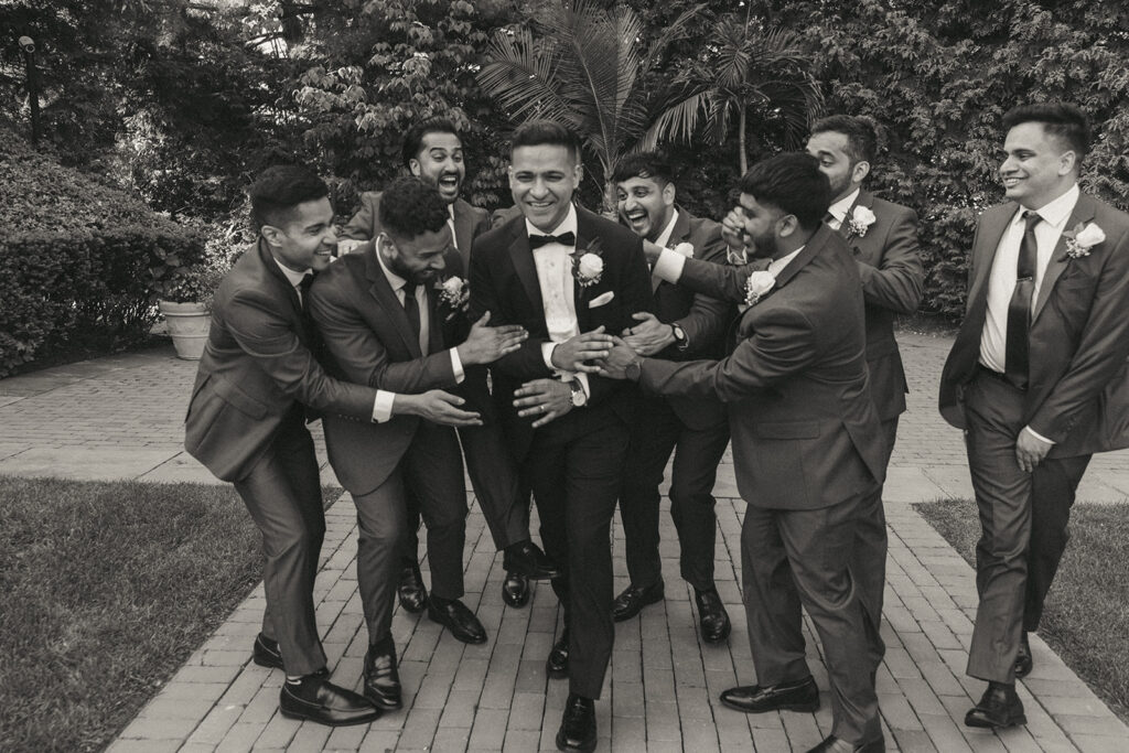 Groom surrounded by groomsmen laughing and joking before the wedding, a fun candid moment captured by Elsie Goodman Photography.