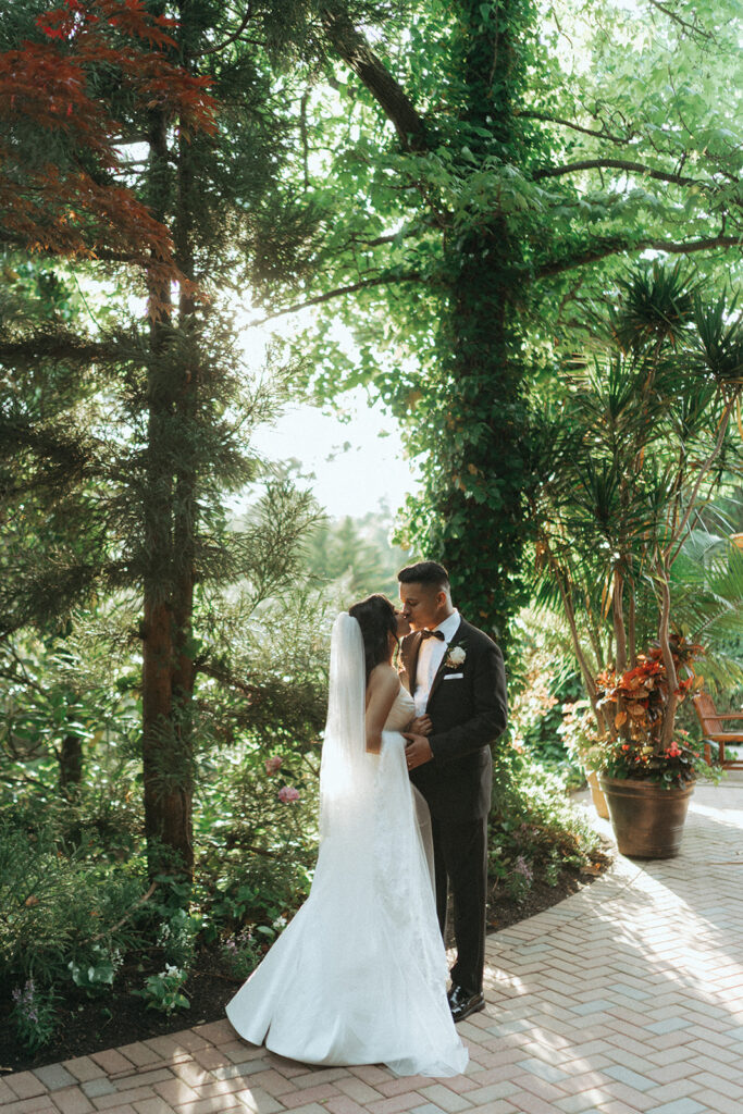 The bride and groom share a romantic kiss under the trees at their Crest Hollow Country Club wedding, captured by Elsie Goodman Photography for their Indian wedding photo gallery.