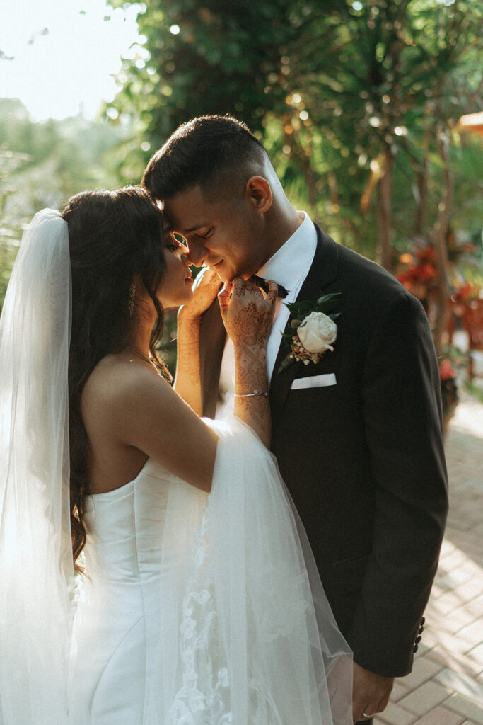 The bride caresses the groom’s face during golden hour at their Catholic Indian wedding at Crest Hollow Country Club, captured by Elsie Goodman Photography.