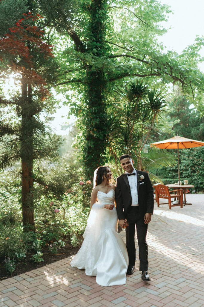 The bride and groom walk hand in hand through lush gardens at their Crest Hollow Country Club wedding, a beautiful Indian wedding venue in Long Island, captured by Elsie Goodman Photography.
