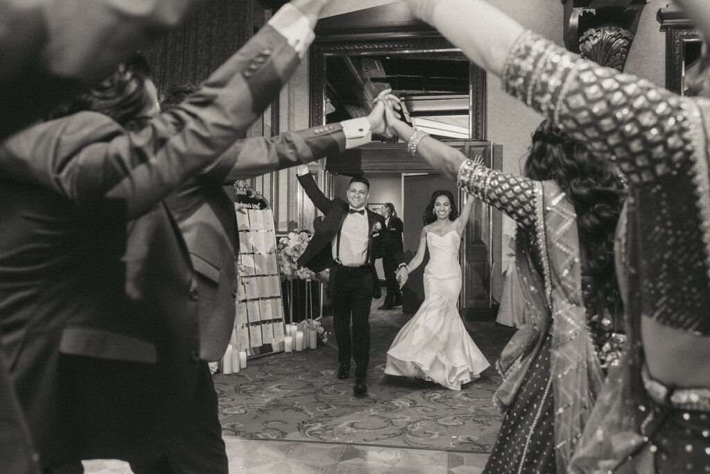 Bride and groom make a triumphant grand entrance through a tunnel of cheering guests at their Crest Hollow Country Club wedding, a joyful highlight of their Catholic Indian wedding story captured by Elsie Goodman Photography for their Long Island wedding photo gallery.