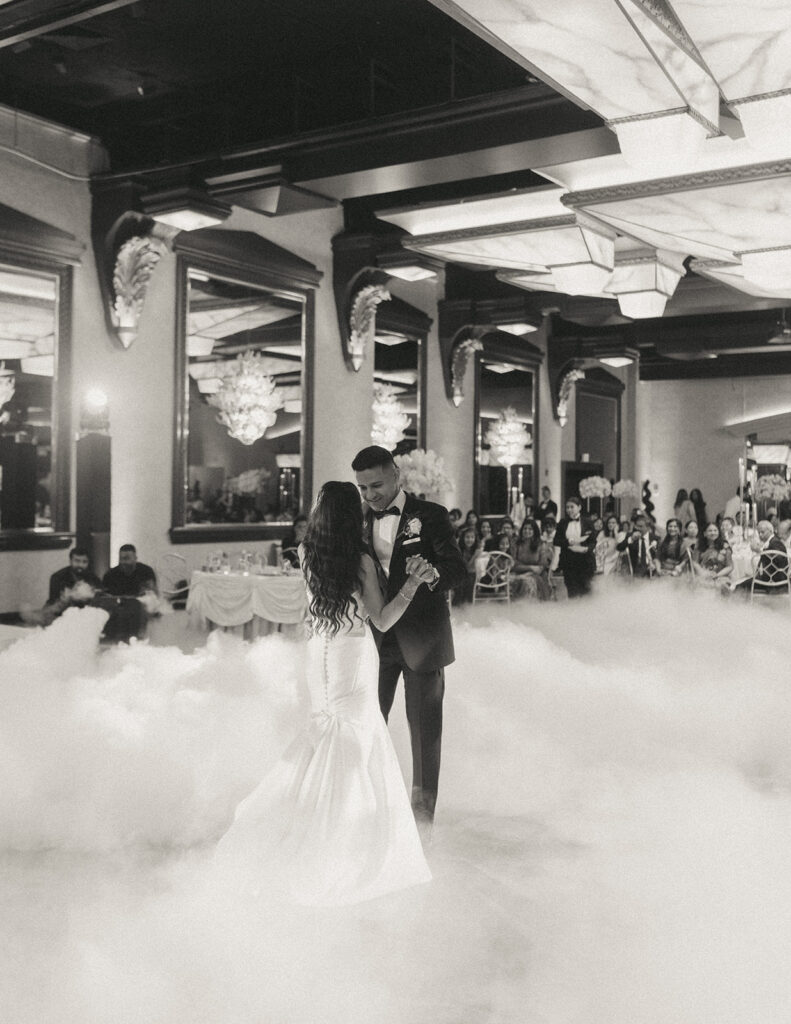 The bride and groom share their first dance surrounded by fog at their elegant Catholic Indian wedding reception at Crest Hollow Country Club, a romantic Long Island wedding moment captured by Elsie Goodman Photography.