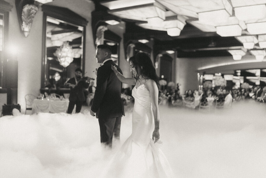 The bride gently taps the groom's shoulder during a playful moment on the dance floor during their first dance surrounded by soft white fog at their Catholic Indian wedding reception at Crest Hollow Country Club, captured by Elsie Goodman Photography.