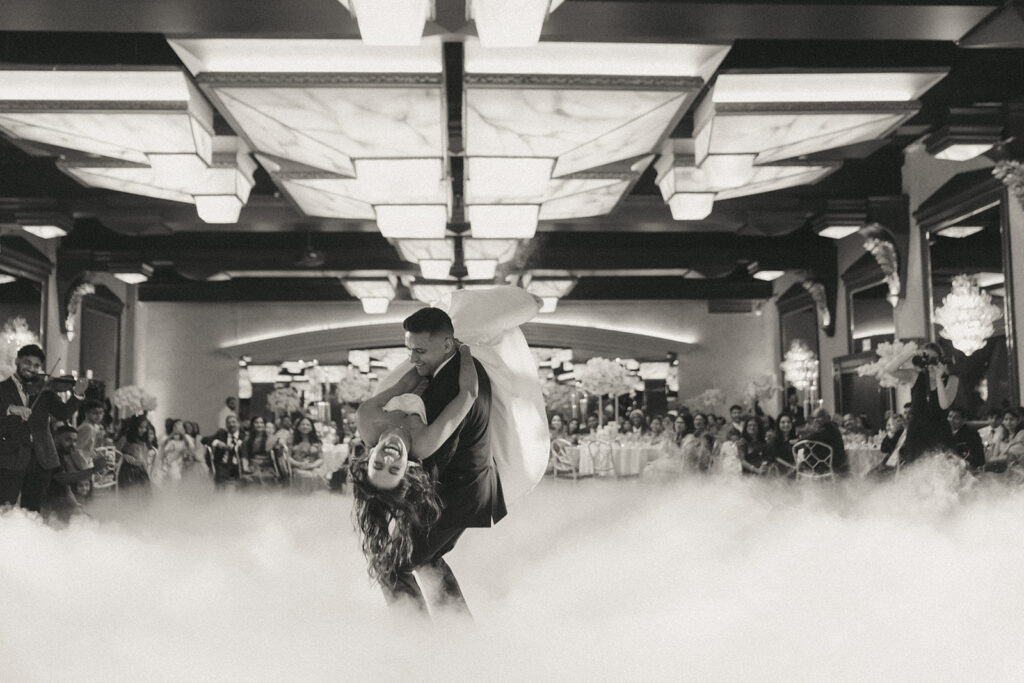 The groom dramatically dips the bride in a romantic moment surrounded by dreamy cloud-like fog on the dance floor at their Crest Hollow Country Club wedding, a magical Catholic Indian wedding moment captured by Elsie Goodman Photography.