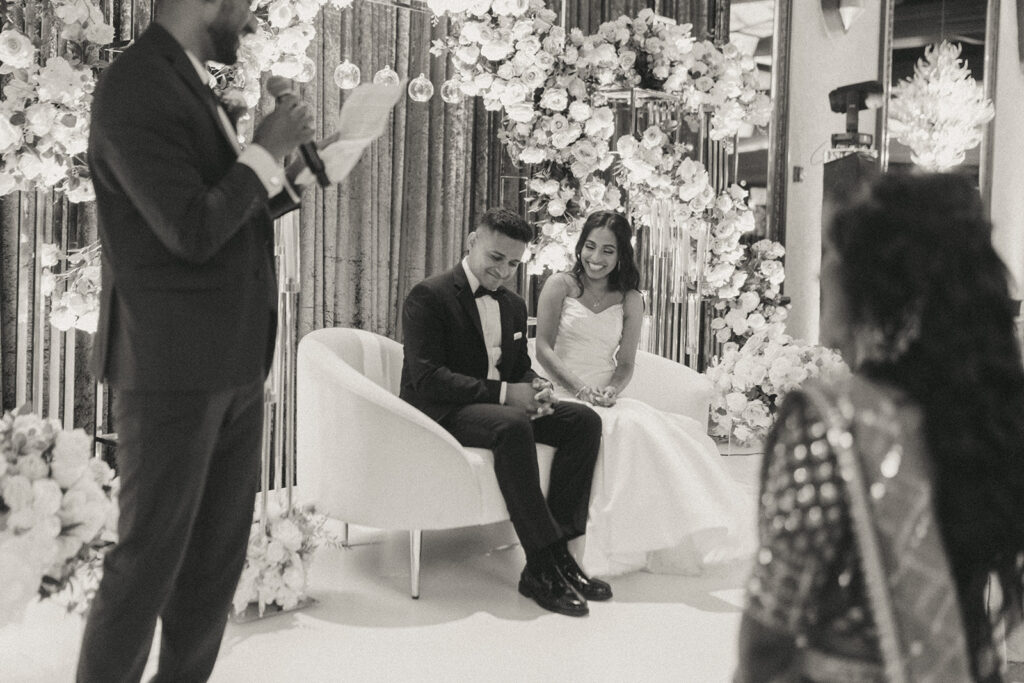 The bride and groom laugh and react during a heartfelt wedding speech at their Catholic Indian wedding at Crest Hollow Country Club, a candid moment captured by Elsie Goodman Photography for a stunning Indian wedding photo gallery.