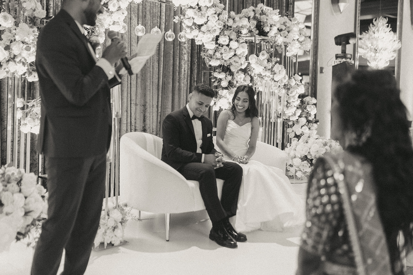 The bride and groom laugh and react during a heartfelt wedding speech at their Catholic Indian wedding at Crest Hollow Country Club, a candid moment captured by Elsie Goodman Photography for a stunning Indian wedding photo gallery.