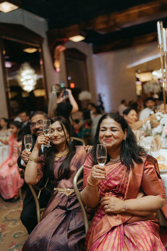 Guests in colorful silk saris raise their champagne glasses for a toast during a joyful Catholic Indian wedding reception at Crest Hollow Country Club, captured by Elsie Goodman Photography for an Indian wedding photo gallery celebrating Long Island weddings.