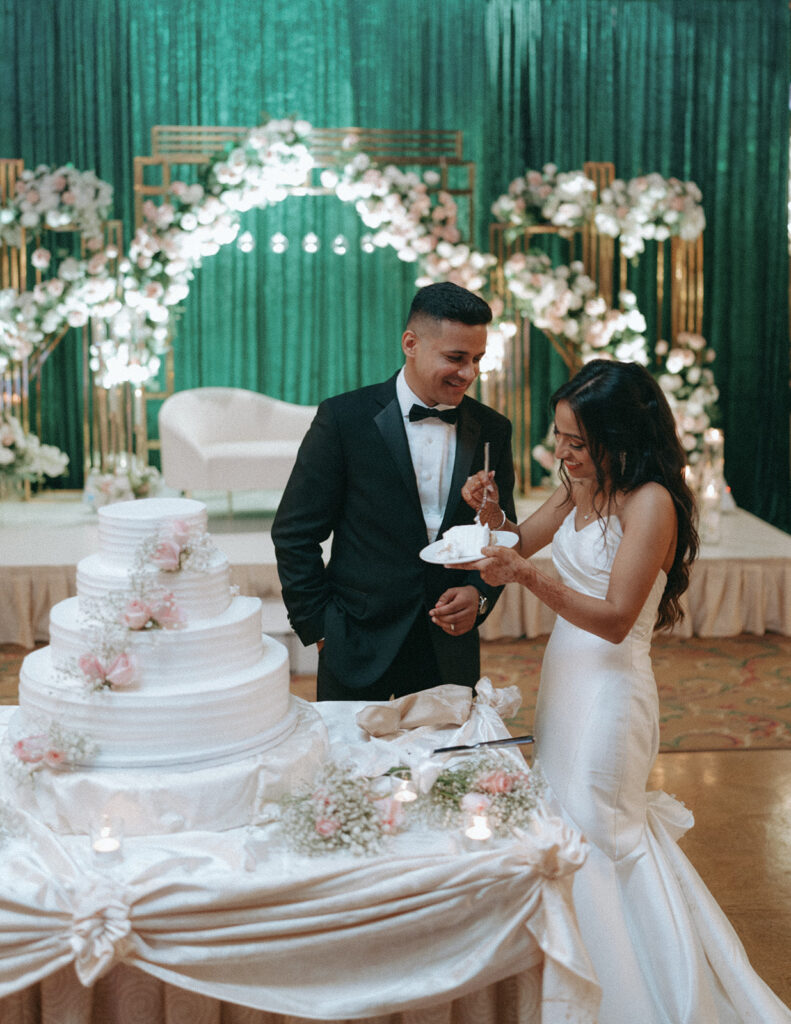 The bride and groom laugh together while sharing cake during their Crest Hollow Country Club wedding, a candid Catholic Indian wedding moment beautifully captured by Elsie Goodman Photography for an Indian wedding photo gallery.