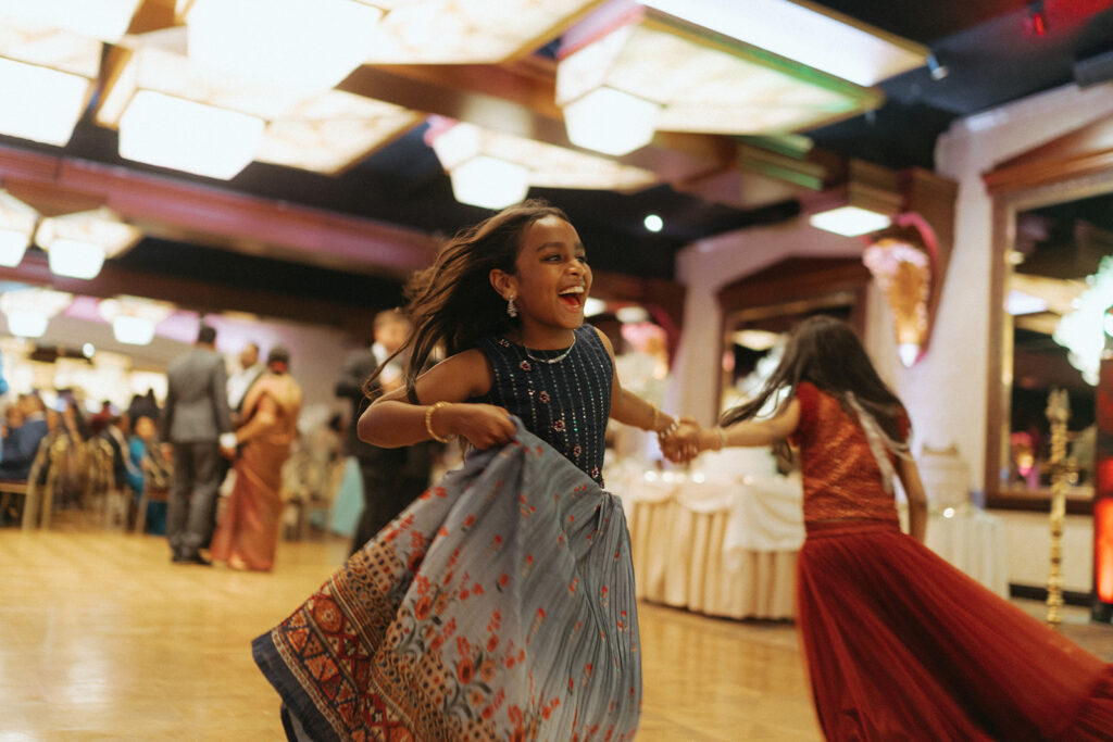 A young girl in a colorful lehenga twirls joyfully on the dance floor during a Catholic Indian wedding reception at Crest Hollow Country Club, a heartwarming moment captured by Elsie Goodman Photography for an Indian wedding photo gallery.