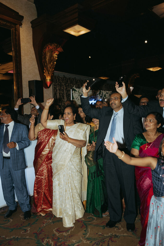 Guests dressed in colorful saris and suits enthusiastically cheer and capture memories during a vibrant Catholic Indian wedding reception at Crest Hollow Country Club, beautifully documented by Elsie Goodman Photography in their Indian wedding photo gallery.