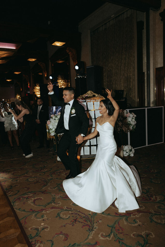 The bride and groom joyfully enter the reception hall hand-in-hand during their Catholic Indian wedding celebration at Crest Hollow Country Club, a perfect moment captured by Elsie Goodman Photography for their Indian wedding photo gallery.