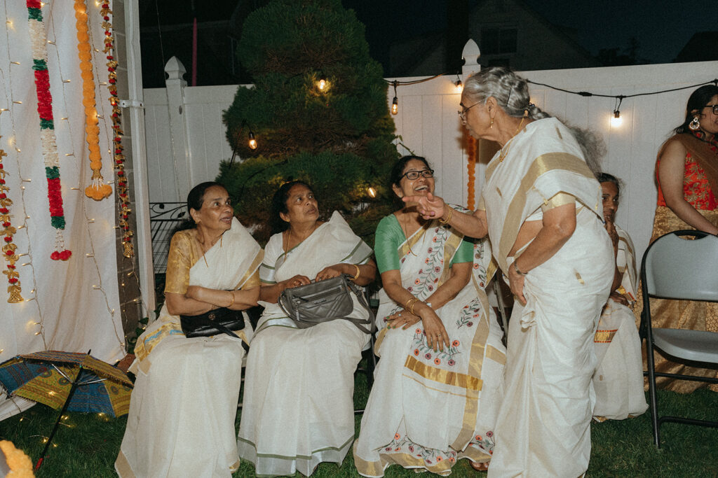 Women in traditional sarees laughing and chatting during Catholic Indian wedding welcome party — Elsie Goodman Photography.