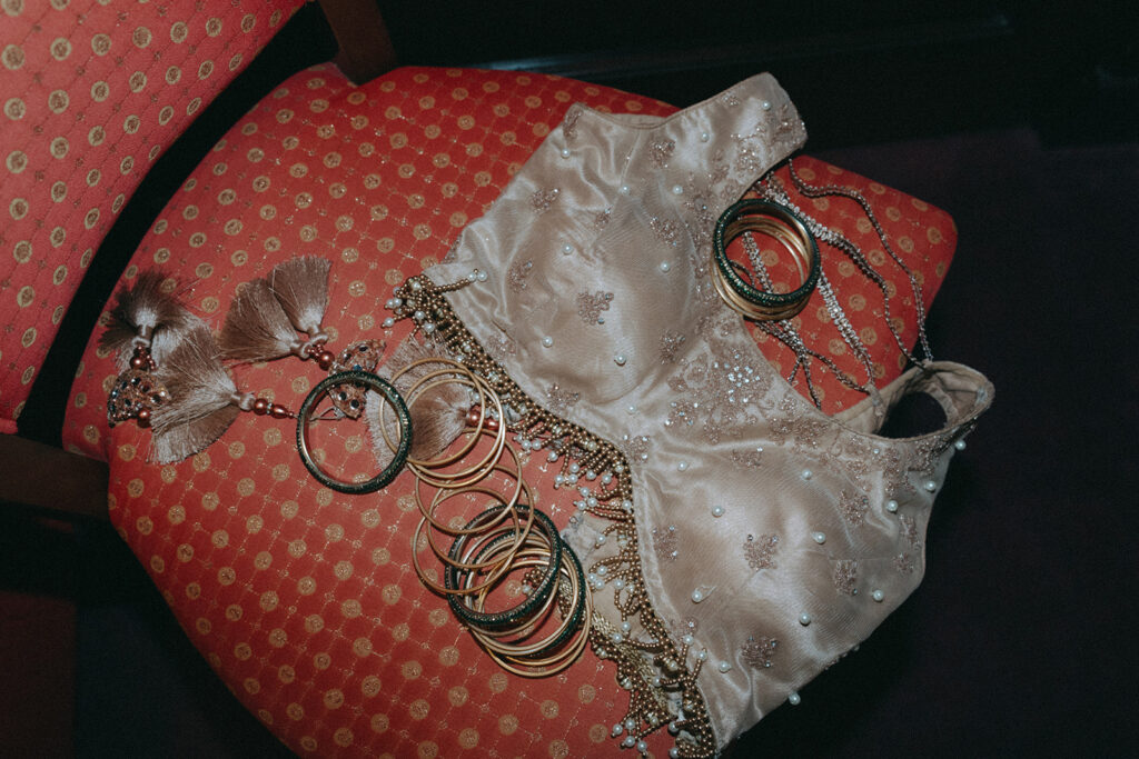 Bridal jewelry and traditional lehenga top arranged on a chair before the Indian Catholic wedding reception at Crest Hollow Country Club, captured by Elsie Goodman Photography.