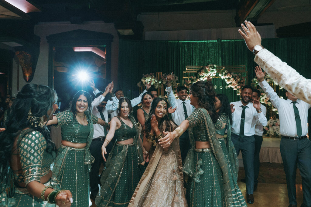 The bride celebrating on the dance floor with her bridesmaids and guests during an Indian Catholic wedding reception at Crest Hollow Country Club, photographed by Elsie Goodman Photography.