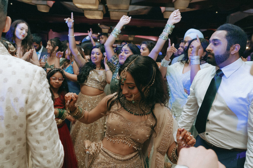 The bride dancing joyfully among friends and family during the Indian Catholic wedding reception at Crest Hollow Country Club, surrounded by guests with raised hands, captured by Elsie Goodman Photography.